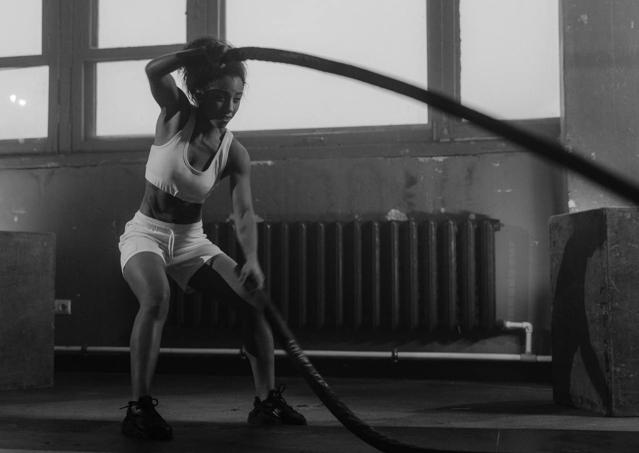 A girl is working out in the gym, a girl in a white top and white shoes is working with ropes, a girl is pumping up her arm muscles